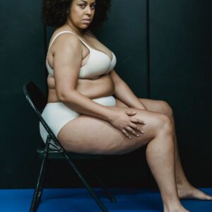 A confident plus-size woman sitting in lingerie, promoting body positivity in a studio setting.