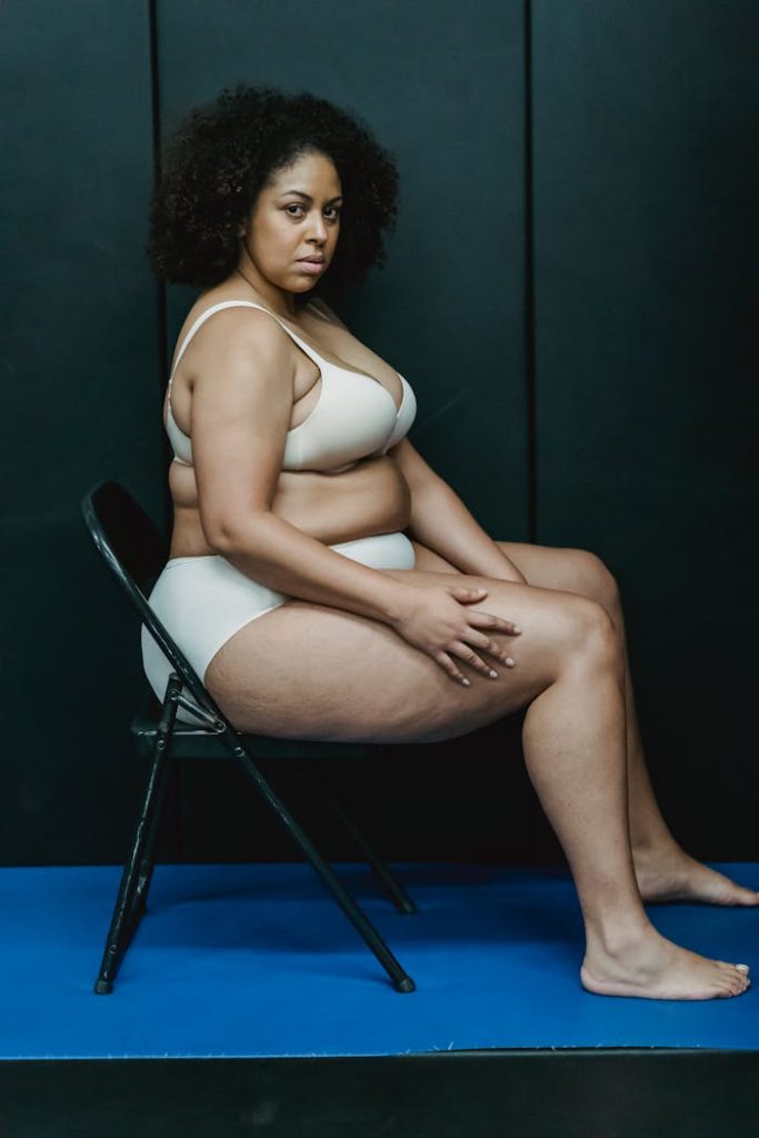 A confident plus-size woman sitting in lingerie, promoting body positivity in a studio setting.